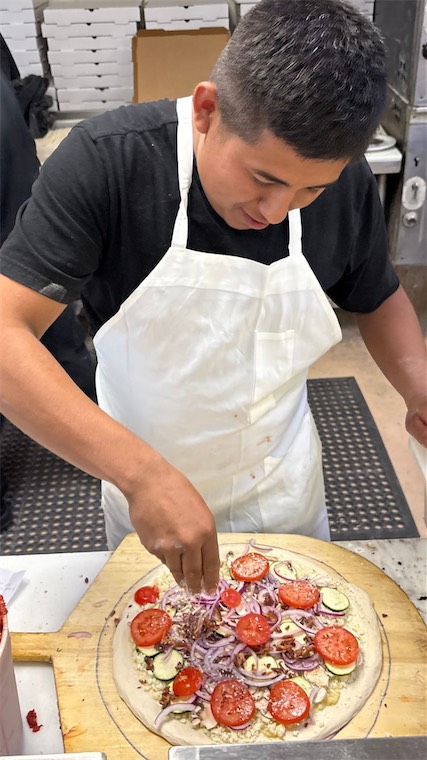 DeVino's cook adding toppings to a pizza