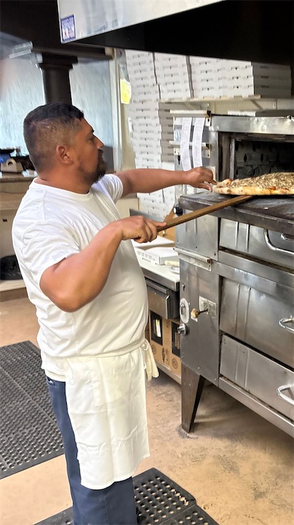 Pizza maker sliding a pizza into the oven
