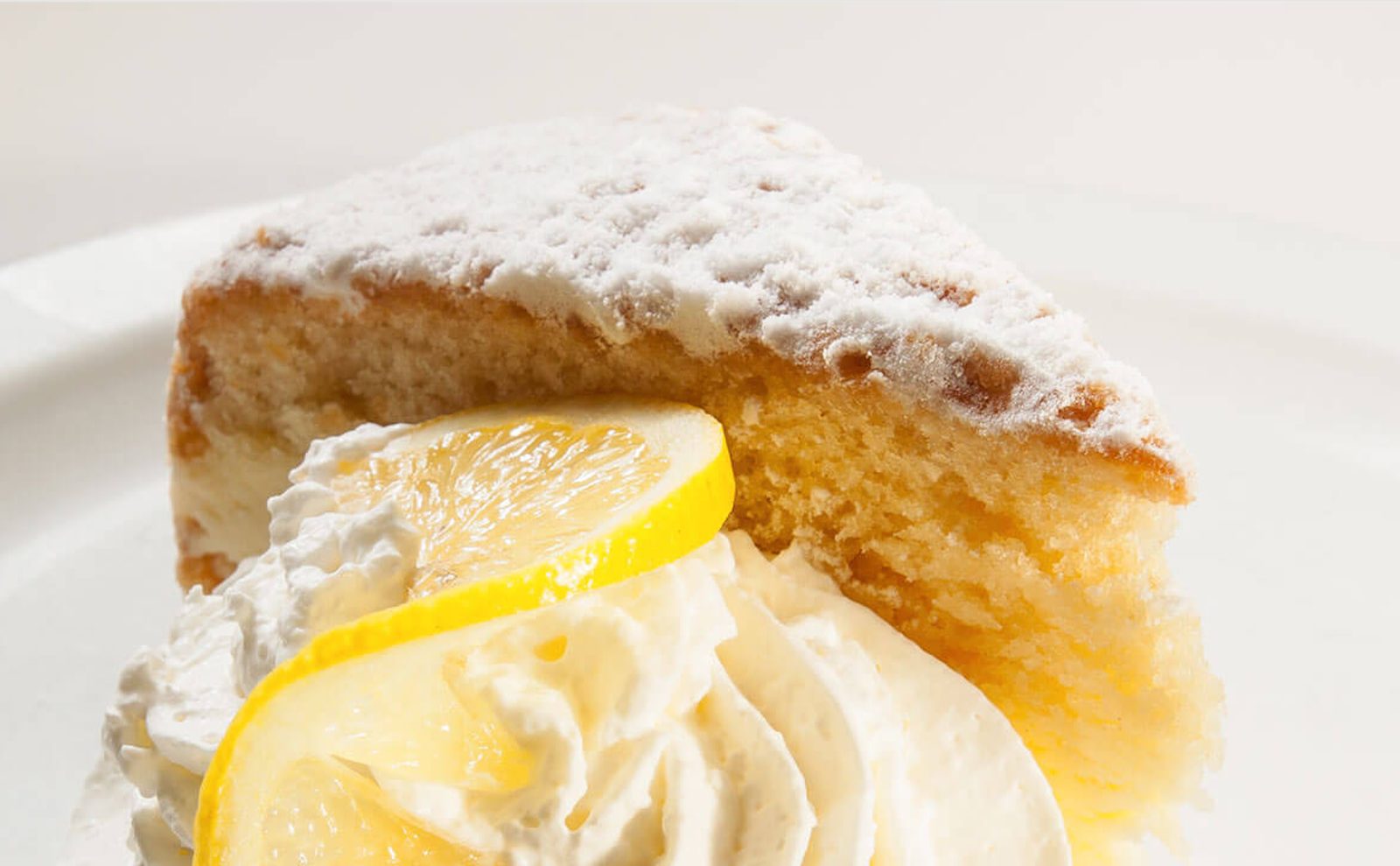 Slice of lemon Italian cream cake with whipped cream and lemon