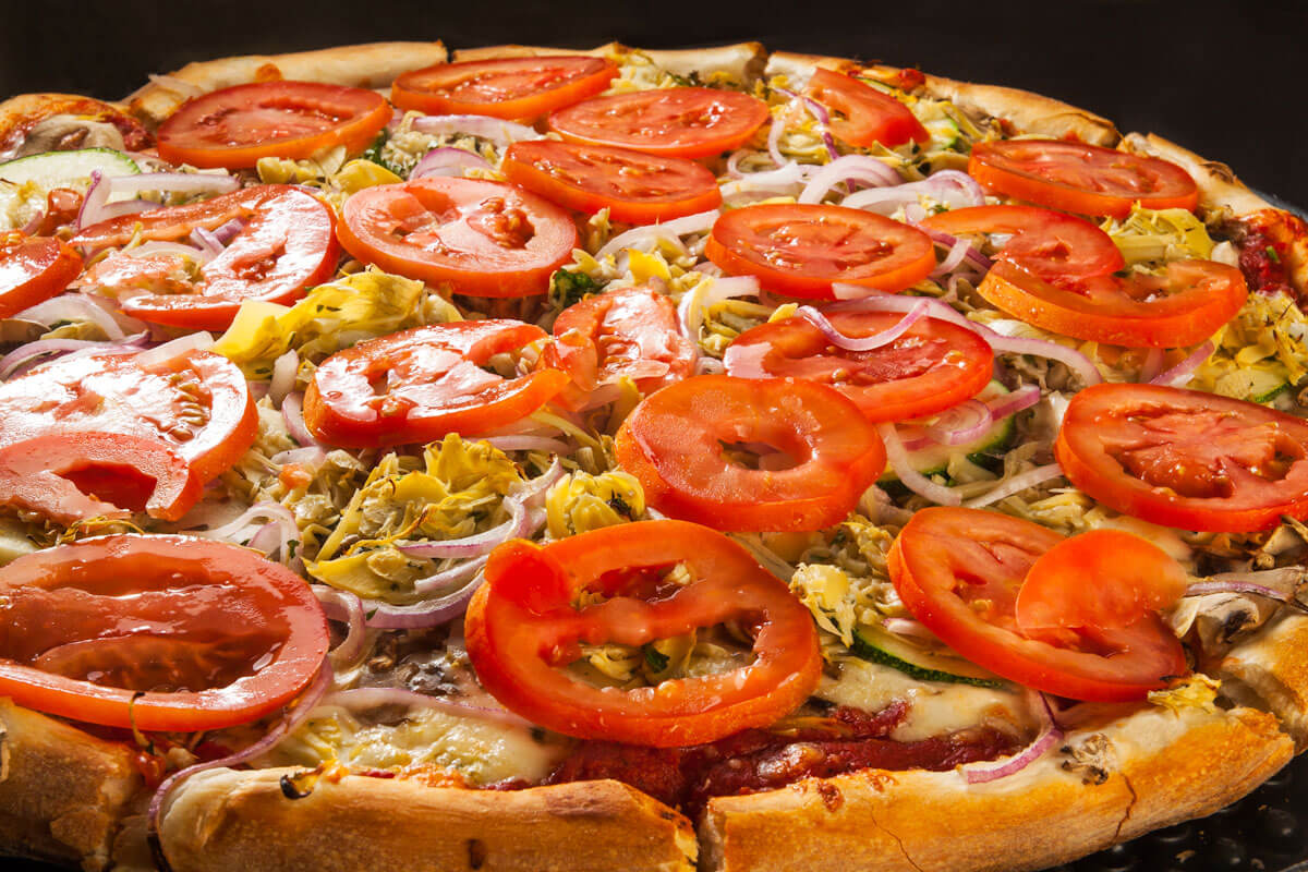 Pizzas being topped with fresh ingredients on a prep counter